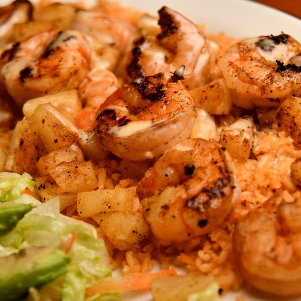 Grilled shrimp and pineapple chunks served over orange rice with a side of lettuce.