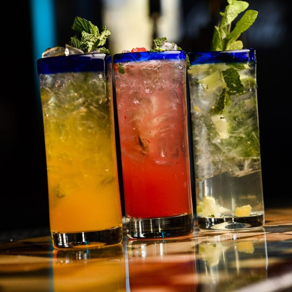 Three vibrant Blue Agave cocktails: yellow, red, and clear, garnished with mint and fruit.